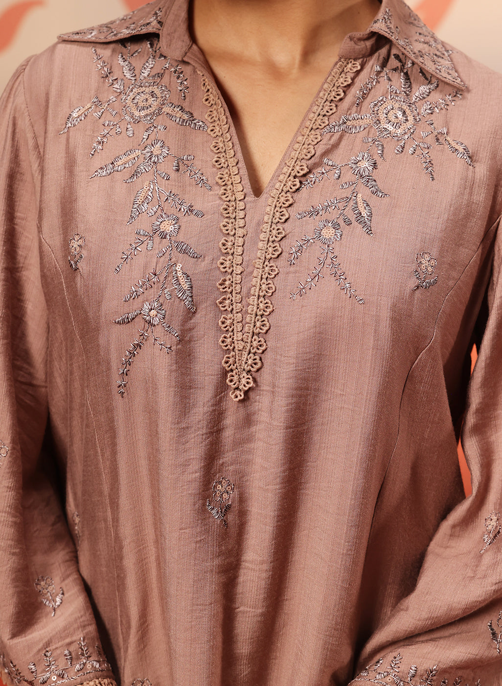 A Woman Seated Wearing a Niya Oak Embroidered Cotton Linen Slub Long Top Featuring Intricate Embroidery With a Rich Brown Color