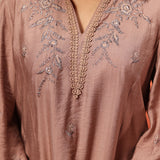 A Woman Seated Wearing a Niya Oak Embroidered Cotton Linen Slub Long Top Featuring Intricate Embroidery With a Rich Brown Color