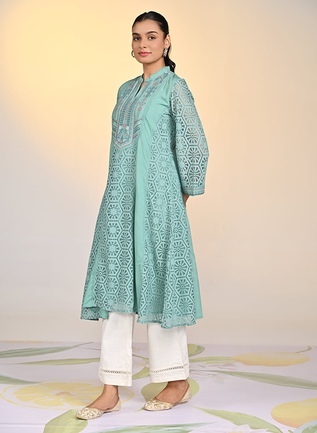 Woman posing in Fariha Carnation Green Embroidered Raschel Net Dress paired with white palazzos and golden pumps