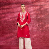 A woman wearing a Saadgi Red Embroidered Cotton Linen Tunic along with a white palazzo