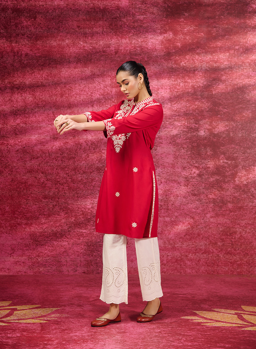 A woman standing wearing a Saadgi Red Embroidered Cotton Linen Tunic paired with a white palazzo