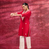 A woman standing wearing a Saadgi Red Embroidered Cotton Linen Tunic paired with a white palazzo